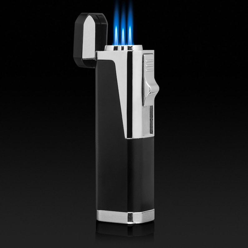 Puede incluir: Un encendedor negro y plateado con tres llamas azules. El encendedor tiene forma rectangular con tapa abatible e interruptor de encendido plateado. El dise&ntilde;o presenta una est&eacute;tica elegante y moderna.