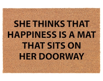 May include: A brown coir doormat with the text "She thinks that happiness is a mat that sits on her doorway" in black lettering.