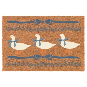 May include: A brown coir doormat with three white geese wearing blue bows. The geese are walking in a line with blue ribbon and bow accents above and below them.