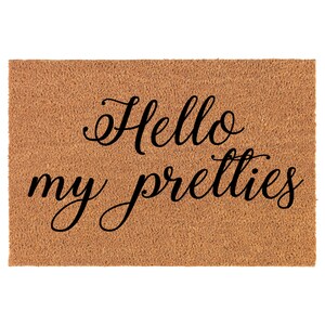 Op de afbeelding: Een rechthoekige deurmat van lichtbruin, getextureerd materiaal. De woorden "Hello my pretties" staan in elegant zwart schrift op de mat. Deze decoratieve mat is ontworpen voor een deuropening.