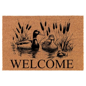 May include: A rectangular doormat with a brown background and a black illustration of ducks in a pond with cattails. The word "WELCOME" is printed in large black letters at the bottom.