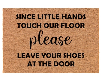 May include: A brown coir doormat with the text "Since little hands touch our floor please leave your shoes at the door" in black.