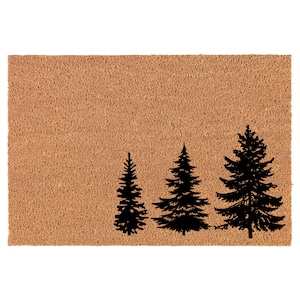 May include: A brown coir doormat with three black silhouette pine trees of varying sizes.