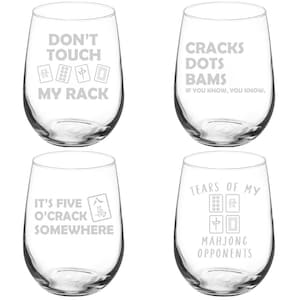 May include: Four clear stemless wine glasses with humorous phrases and Mahjong tile graphics etched on them. The phrases include "Don't Touch My Rack," "Cracks Dots Bams," "It's Five O'Crack Somewhere," and "Tears of My Mahjong Opponents."