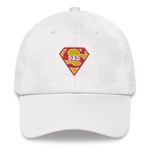 May include: White baseball cap with an embroidered red and yellow Superman logo that says "DAD" in the center.