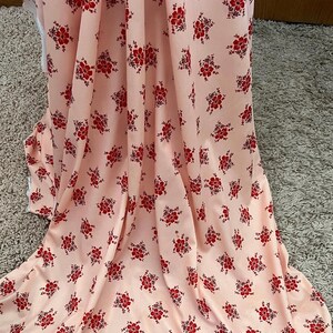 May include: A pink fabric with a repeating pattern of small red flowers. The fabric is folded and draped over a surface.