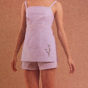 May include: A light purple gingham sleeveless top with a matching pair of shorts. The top has a small floral embroidery on the side.
