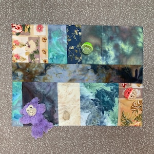 May include: A patchwork quilt made of various fabrics in shades of blue, green, and brown. The quilt features a purple stuffed animal, a green ball, and a red and white ball.