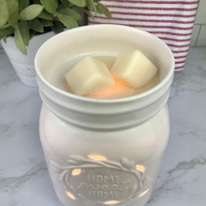 Pode incluir: Aquecedor de cera branco de cer&acirc;mica em forma de jarro com um design recortado que diz "Home Sweet Home". Duas ceras brancas est&atilde;o no aquecedor.