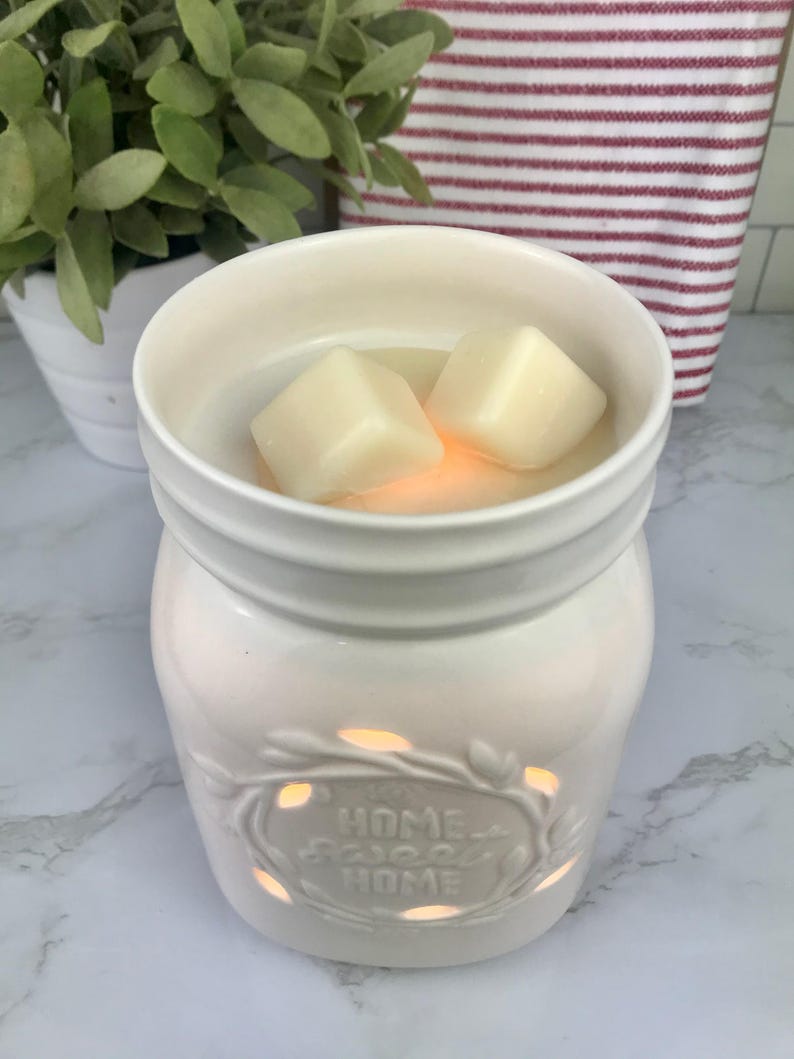 Pode incluir: Aquecedor de cera branco de cer&acirc;mica em forma de jarro com um design recortado que diz "Home Sweet Home". Duas ceras brancas est&atilde;o no aquecedor.