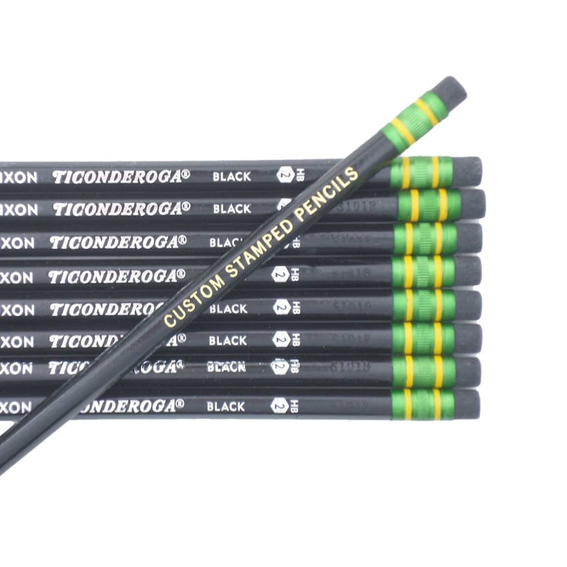 以下が含まれることがあります： 緑と黄色のストライプの入った黒い鉛筆の束。鉛筆には「Ticonderoga」と「Custom Stamped Pencils」のラベルが貼られています。