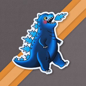 May include: A blue cartoon monster with a spiky back and a small flame coming out of its mouth. The monster has a pink blush on its cheeks.