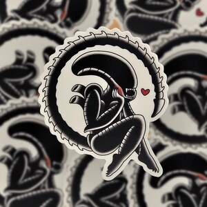 Peut inclure: Autocollant noir et blanc repr&eacute;sentant un extraterrestre stylis&eacute; avec un c&oelig;ur. L'alien est repr&eacute;sent&eacute; dans une pose assise avec une queue incurv&eacute;e, entour&eacute; d'une bordure blanche. Le design a une esth&eacute;tique inspir&eacute;e du tatouage.
