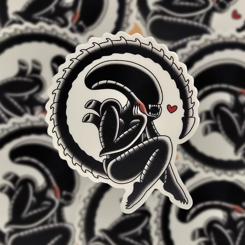 Peut inclure: Autocollant noir et blanc repr&eacute;sentant un extraterrestre stylis&eacute; avec un c&oelig;ur. L'alien est repr&eacute;sent&eacute; dans une pose assise avec une queue incurv&eacute;e, entour&eacute; d'une bordure blanche. Le design a une esth&eacute;tique inspir&eacute;e du tatouage.