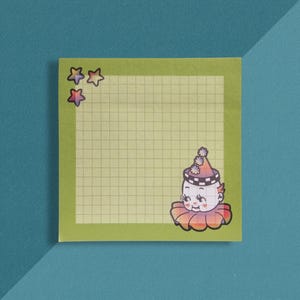 May include: A square olive green sticky note featuring a light green grid pattern in the center. The top left corner displays three small gradient stars. The bottom right corner features a cartoon clown head wearing a ruffled collar and hat.