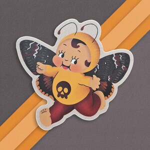 May include: A yellow and black butterfly sticker with a skull design. The butterfly has a human-like face with a big smile.