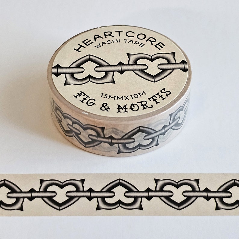 May include: A roll of beige washi tape labeled HEARTCORE WASHI TAPE and FIG & MORTIS with a 15mm x 10m dimension. The tape features a repeating black and grey graphic pattern of heart-shaped chain links connected by straight metal bars.