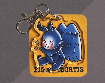 May include: A clear acrylic keychain featuring a blue moth-like creature with red eyes and wings, attached to a silver metal lobster clasp. The keychain is mounted on a square yellow backing card with the text FIG AND MORTIS printed in black.