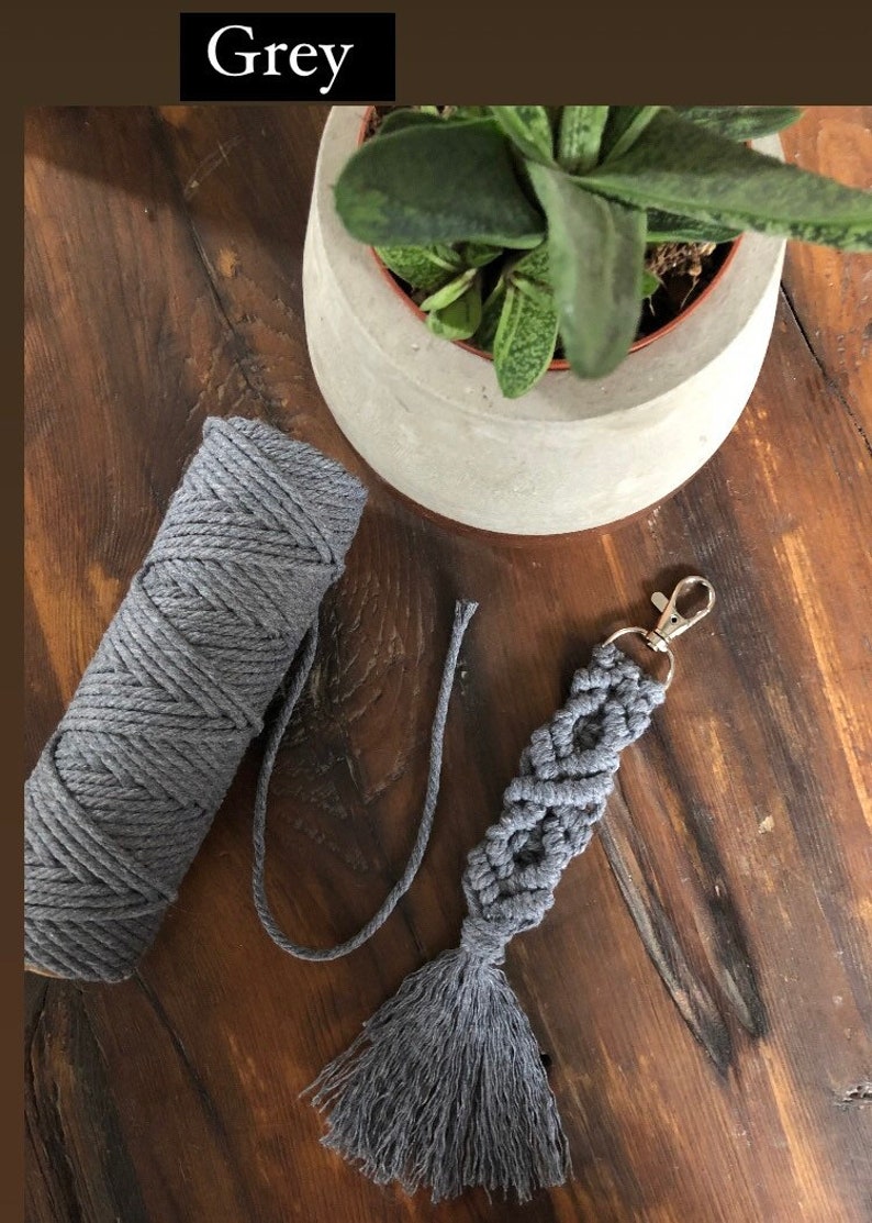 May include: Grey macrame keychain with a tassel and a silver key ring. The keychain is made with a thick grey cord and is shown next to a ball of grey cord.