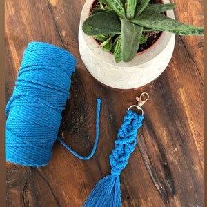 May include: Sea blue macrame keychain with a tassel. The keychain is made with a thick blue cord and has a silver key ring.
