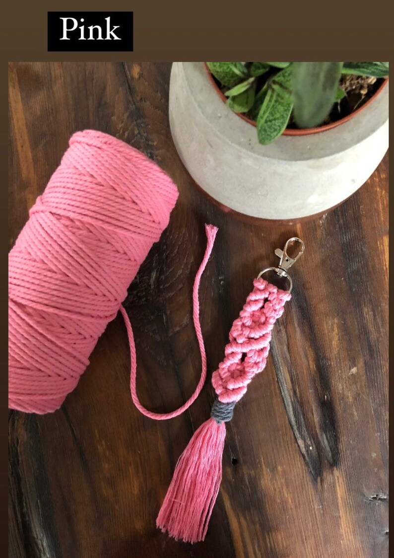May include: Pink macrame keychain with a tassel. The keychain is made with pink and grey cord and has a silver key ring.