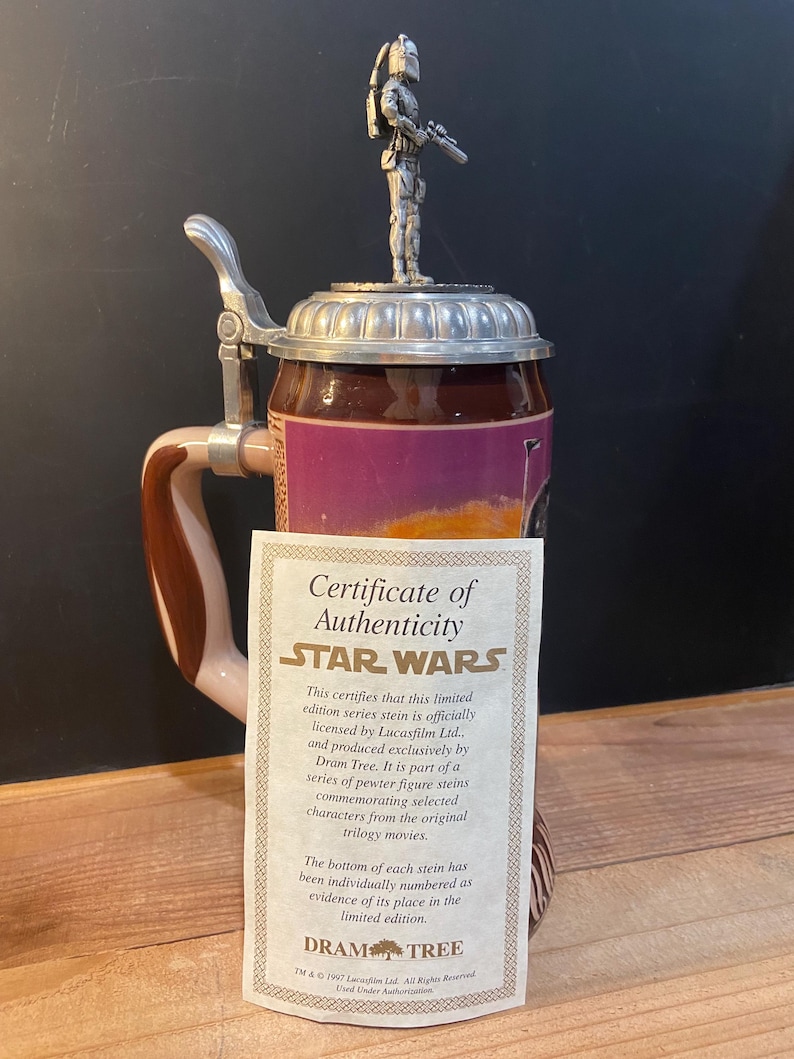 May include: A Star Wars themed beer stein with a pewter figure on the lid. The stein has a brown and tan handle and a certificate of authenticity. The stein is a limited edition item.