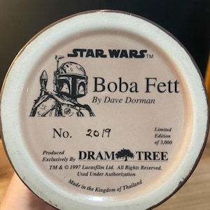 May include: A ceramic mug base featuring the Star Wars logo and a Boba Fett illustration. The text reads "Boba Fett by Dave Dorman" and "No. 2019, Limited Edition of 3,000." Produced exclusively by Dram Tree. Made in Thailand.