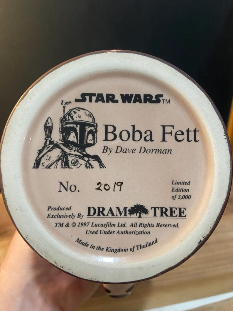 May include: A ceramic mug base featuring the Star Wars logo and a Boba Fett illustration. The text reads "Boba Fett by Dave Dorman" and "No. 2019, Limited Edition of 3,000." Produced exclusively by Dram Tree. Made in Thailand.