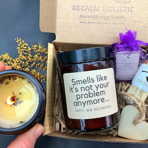 Pode incluir: Um conjunto de presente com uma vela de soja marrom, uma bolsa roxa de sais de banho, uma pequena garrafa de vidro com f&oacute;sforos e um cora&ccedil;&atilde;o de madeira. O r&oacute;tulo da vela diz "Smells like it's not your problem anymore... Happy New Beginnings".