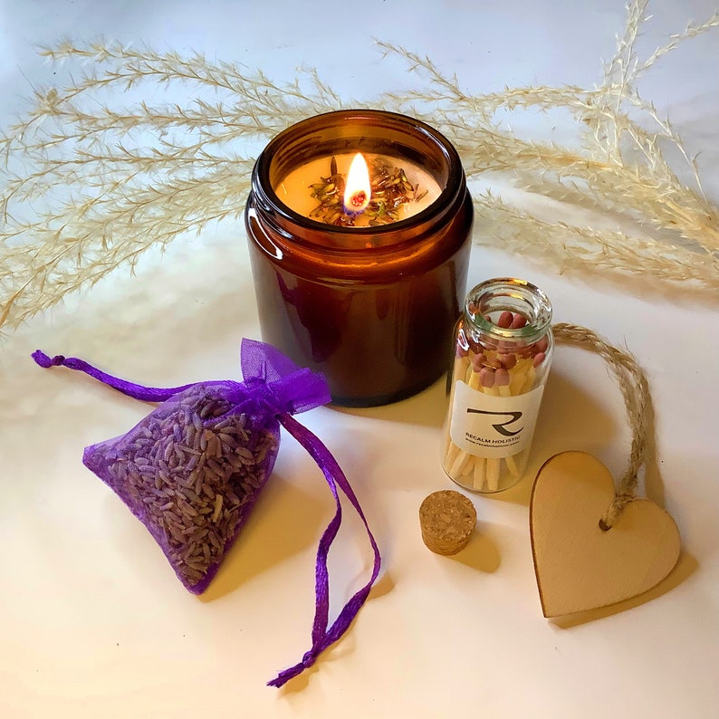 Pode incluir: Uma vela de vidro marrom com um pavio aceso e aroma de lavanda, uma bolsa de cord&atilde;o roxo cheia de bot&otilde;es de lavanda, uma pequena garrafa de vidro com f&oacute;sforos e um cora&ccedil;&atilde;o de madeira.