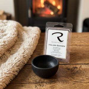 May include: A small black matte bowl sits next to a clear plastic clamshell package of Italian Garden aromatherapy soy and coconut wax melts. The label features the Recalm Holistic logo and lists ingredients including bay laurel, rosemary, and lemon.