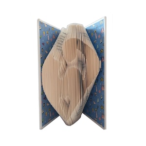 May include: A book folded into a 3D sculpture of a person. The book has a blue cover with a pattern of colorful illustrations.