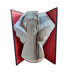 Puede incluir: Un libro doblado en forma de ángel. El ángel es blanco y el libro está encuadernado en rojo y negro.