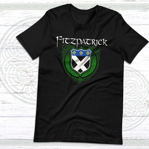 May include: Black t-shirt with a green Celtic knot design and a white shield with a blue and white cross and three gold fleurs-de-lis. The text "Fitzpatrick" is above the shield.