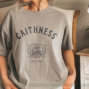 Puede incluir: Una camiseta gris con un estampado gráfico de un barco y el texto "CAITHNESS GALLAIBH SCOTLAND"