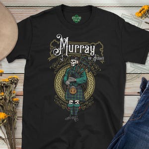 May include: Black t-shirt with a skeleton bagpiper in a green jacket and tartan kilt. The shirt displays "Murray of Atholl" in a decorative font, surrounded by Celtic knotwork. The t-shirt is from Celtic Folk.
