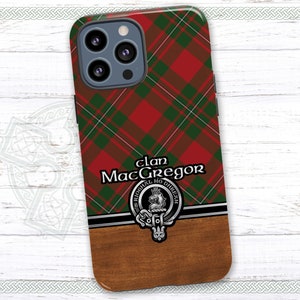 May include: A red and green tartan phone case with a wood grain design. The case features a crest with the text "Clan MacGregor" and the motto "E rioghail mo dhream".