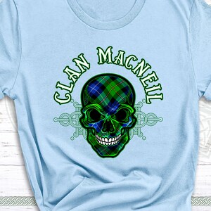 May include: A light blue t-shirt with a green and blue skull design. The skull is wearing a tartan pattern. The text "Clan MacNeil" is written in a green and white font above the skull.