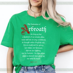 May include: Green t-shirt with a white graphic print of the Declaration of Arbroath, a historical document from Scotland. The text reads: "As long as but a hundred of us remain alive, never will we on any conditions be brought under English rule. It is in truth not for glory, nor riches, nor honours that we are fighting, but for freedom - for that alone, which no honest man gives up but with life itself. April 6, 1320."