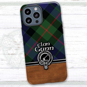May include: A phone case with a green, blue, and red tartan pattern. The case has a silver clan crest with the text "Clan Gunn" and the motto "Gut Pax Aut Bellum". The back of the case is a wood grain pattern.