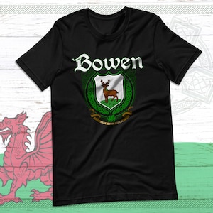 Könnte beinhalten: Schwarzes T-Shirt mit dem Namen "Bowen" in Weiß, über einem grün-weißen Wappen mit einem Hirsch. Das T-Shirt hat einen Rundhalsausschnitt und kurze Ärmel. Der Hintergrund zeigt die walisische Flagge und keltische Knotenmuster.