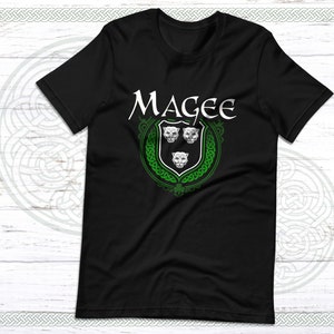 May include: Black t-shirt featuring a white graphic of a Celtic knot design with three white wolf heads inside. The text "MAGEE" is above the design in white.