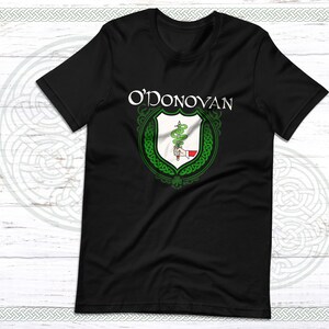 May include: Black t-shirt featuring a green Celtic knot design and the text "O'DONOVAN" in white. The design includes a shield with a snake and a hand holding a sword.