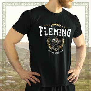 May include: Black t-shirt with a gold graphic of a man in a kilt and the text "Clan Fleming Let the Deed Shaw".