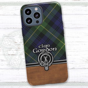 May include: A phone case with a blue, green, and yellow plaid pattern. The case has a silver crest with a stag and the text "Clan Gordon Byddand". The case has a wood-grain design on the bottom half.