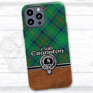 May include: A green, blue, and red plaid phone case with a crest featuring a crane and the text "Clan Cranston" in black. The case has a wood-grain design on the bottom.