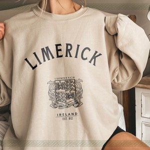 May include: A beige sweatshirt with the text "LIMERICK" in black, a crest with the text "LUIMNEACH" and "IRELAND EST. 812" below it.