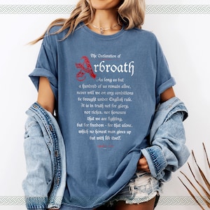 May include: A blue t-shirt with a white graphic print of the Declaration of Arbroath. The text reads: "As long as but a hundred of us remain alive, never will we on any conditions be brought under English rule. It is in truth not for glory, nor riches, nor honours that we are fighting, but for freedom - for that alone, which no honest man gives up but with life itself."