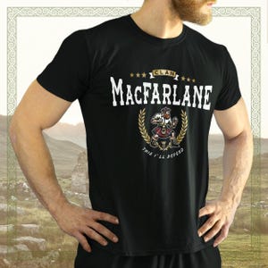 Puede incluir: Camiseta negra con un gráfico blanco de un guerrero escocés con kilt, sosteniendo una espada y un escudo. El gráfico dice "Clan MacFarlane" y "This I'll Defend".