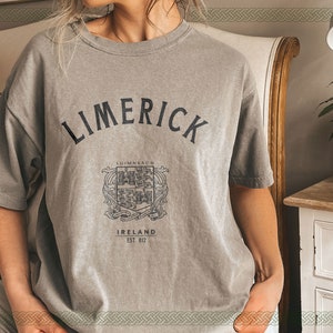 May include: A gray t-shirt with the text "LIMERICK" in black lettering. The shirt also features a black and white crest with the text "Limerick" and "Ireland Est 812".